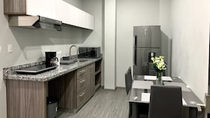 Cocina compacta con encimera de granito, microondas integrado y refrigerador de acero inoxidable.