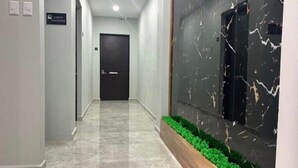 Un pasillo moderno con piso de mármol, un letrero que indica lavandería para huéspedes y una maceta con follaje verde.