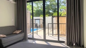 Una habitación de hotel moderna con sofá, cama grande y puerta corrediza de vidrio que da a un área exterior con piscina y pared de ladrillo.