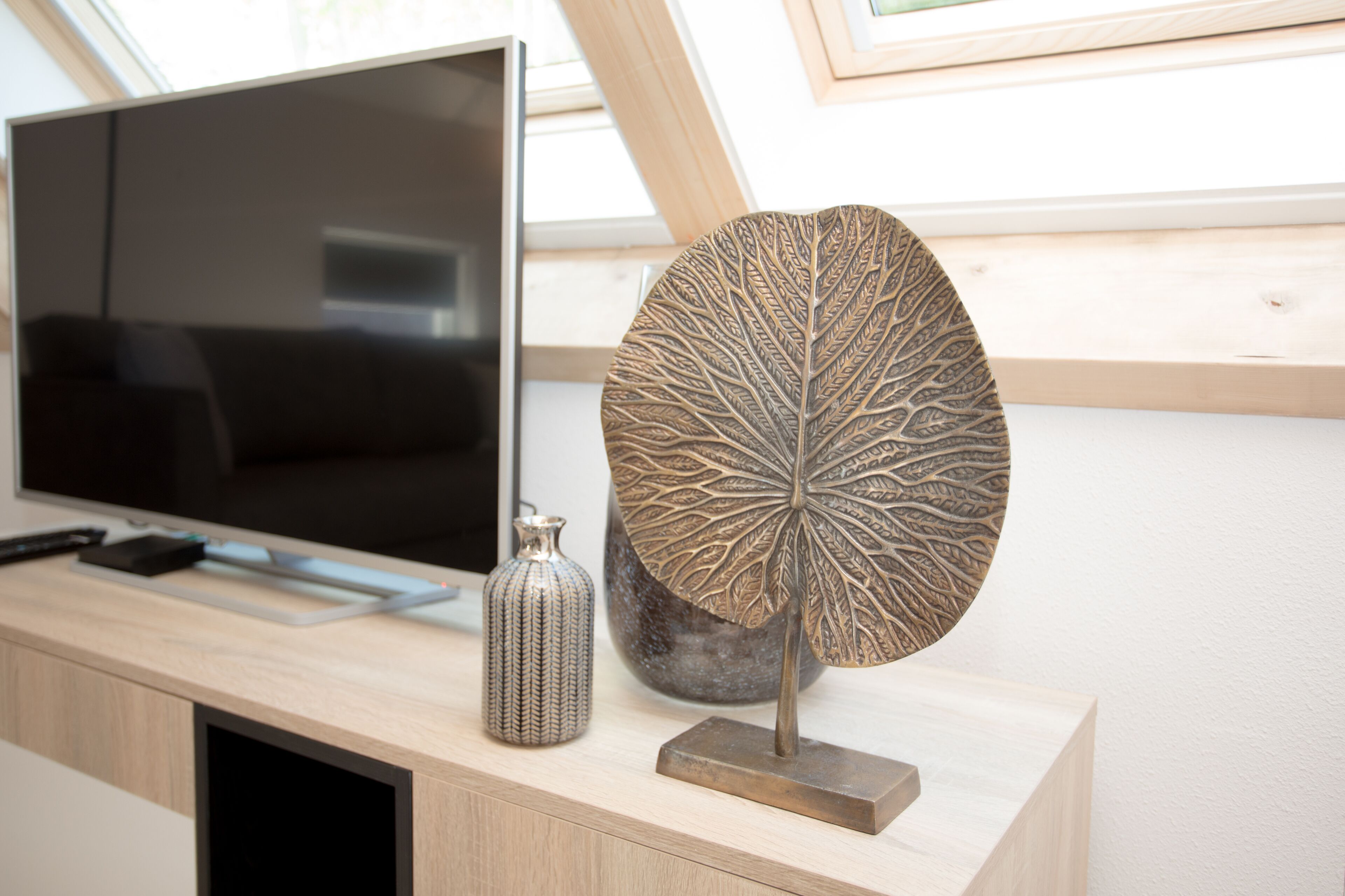 Een moderne woonkamer met een flatscreen-televisie, een decoratieve bladsculptuur en een gevlekte vaas op een houten console.