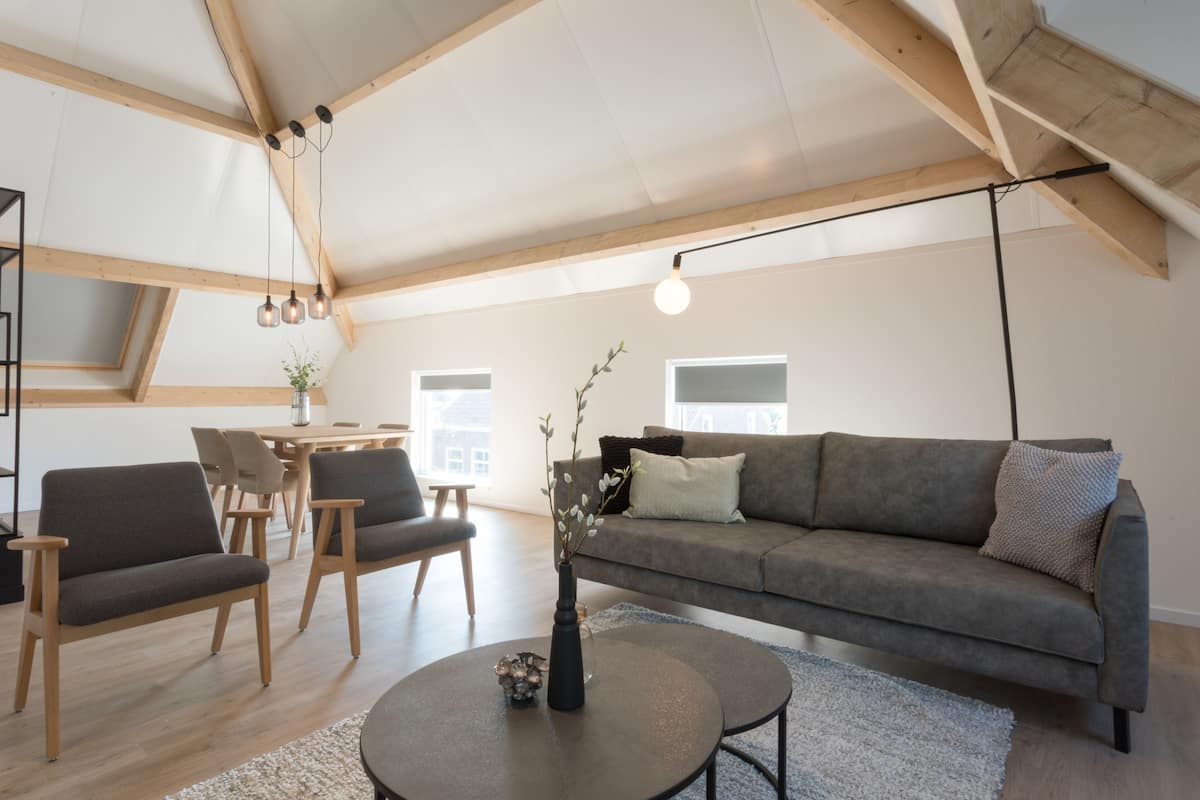 Una sala de estar moderna con un sofá gris, sillas de madera, una mesa de centro redonda y un tragaluz.