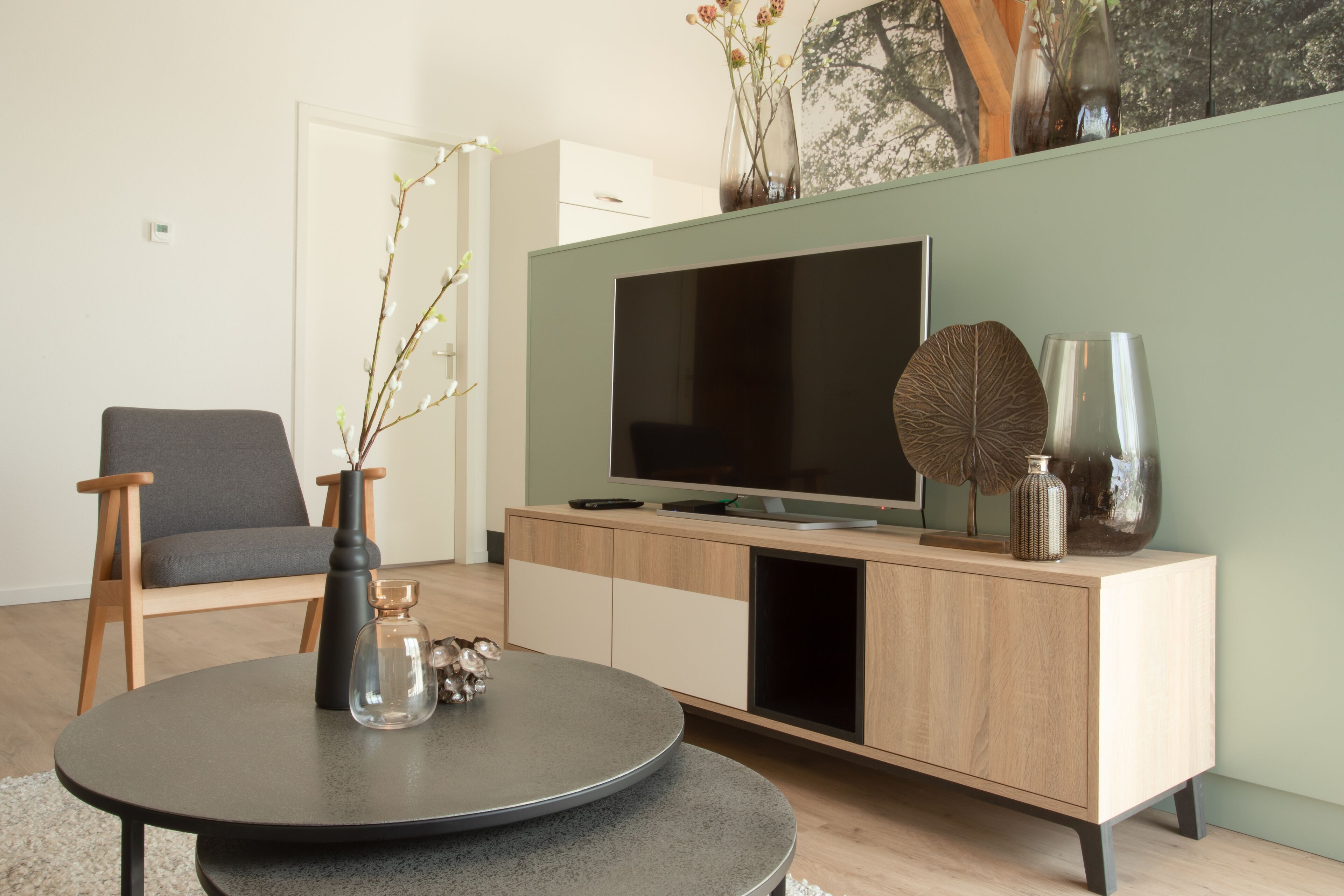 A modern living room with a round table, a grey sofa, a wooden TV stand, and decorative vases.