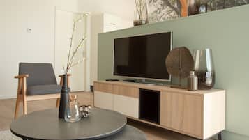 A modern living room with a round table, a grey sofa, a wooden TV stand, and decorative vases.