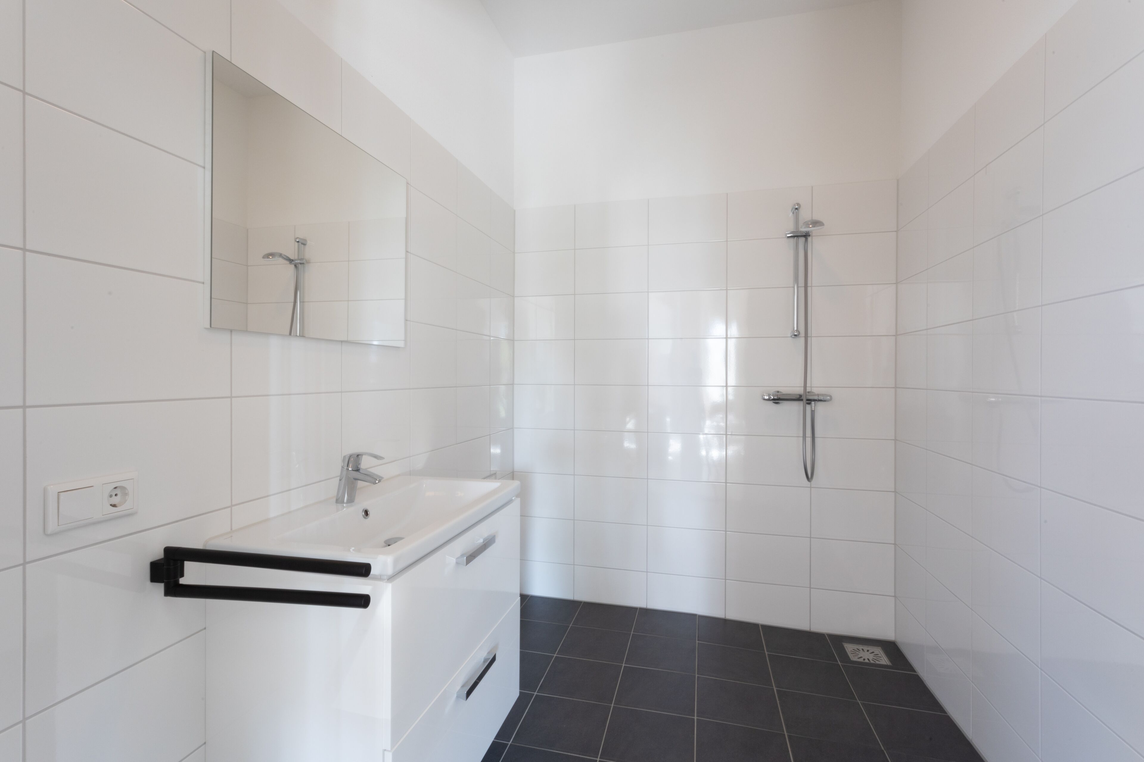 Une salle de bain moderne avec des carreaux blancs, un lavabo, un miroir et une douche.