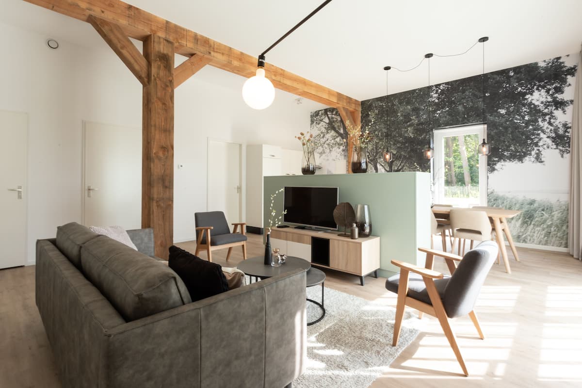 Una sala de estar moderna con un sofá gris, vigas de madera, un televisor y un comedor con una mesa y sillas.