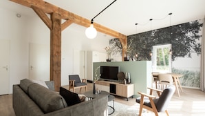 A modern living room with a grey sofa, wooden beams, a TV, and a dining area with a table and chairs. - Hofstede Moesbosch l Kloeg Collection (Koudekerke)