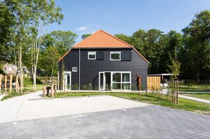 Ett modernt hus i två våningar med en mörk fasad, ett rött tegeltak och en grusuppfart.