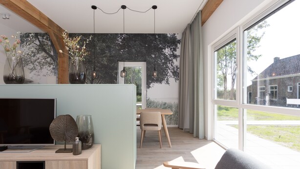 A modern living room with a TV, wooden furniture, and large windows offering a view of a house. - Hofstede Moesbosch l Kloeg Collection (Koudekerke)