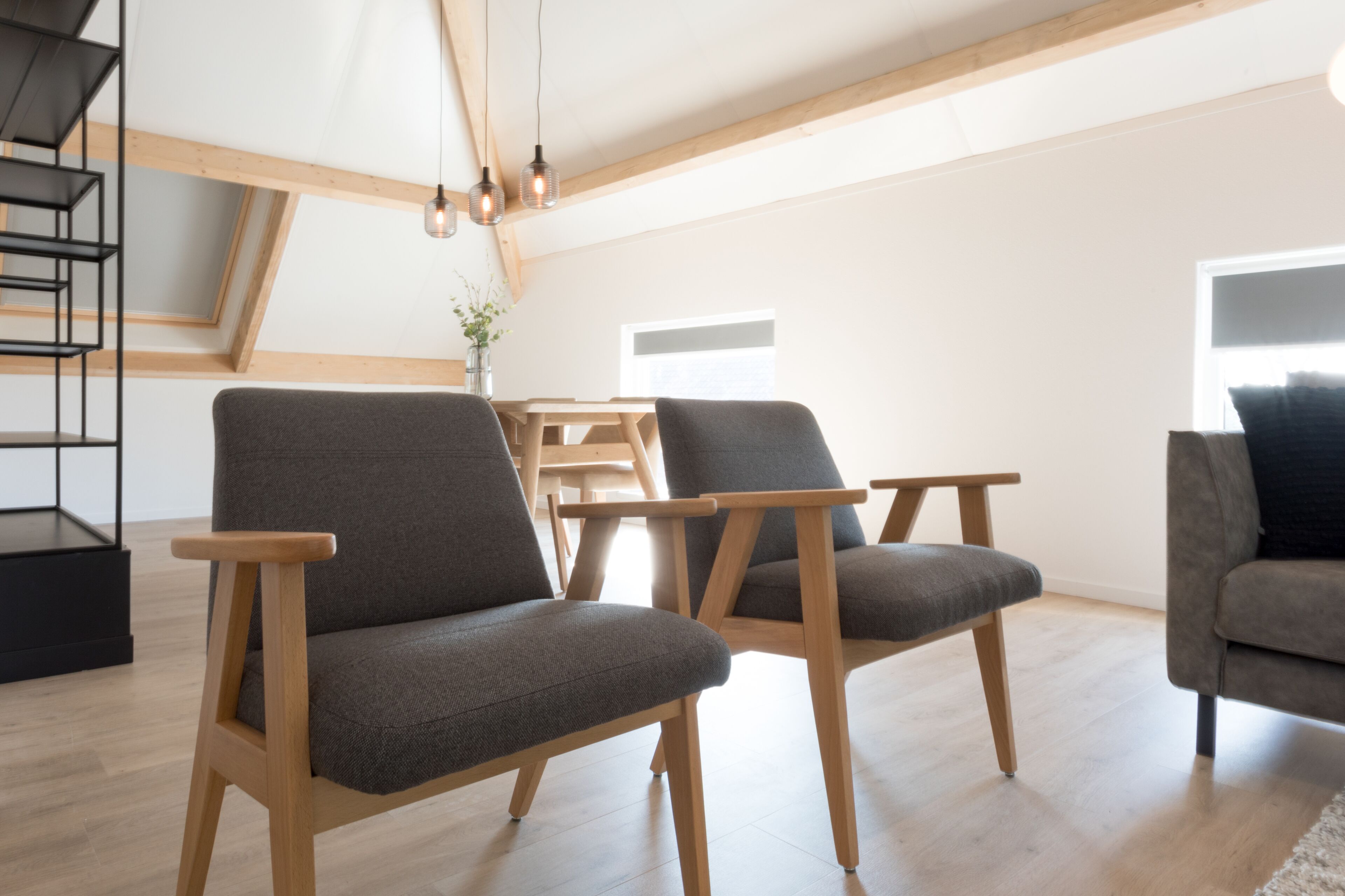 Ein modernes Wohnzimmer mit Holzboden, grau gepolsterten Sesseln, einem Holztisch und einer Treppe mit schwarzer Geländer.