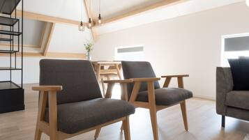 A modern living room with wooden flooring, grey upholstered chairs, a wooden coffee table, and a staircase with a black railing.