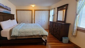 A bedroom with a wooden bed, a dresser, and a mirror. There are two doors and a window with curtains. - Our Cottage Unit-Private end unit of Yellowstone Basin Inn (Gardiner)