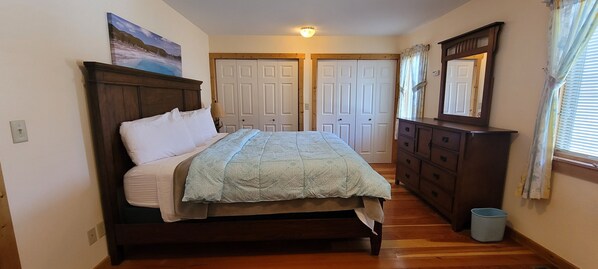 Een slaapkamer met een houten bed, een dressoir en een spiegel. Er zijn twee deuren en een raam met gordijnen.
