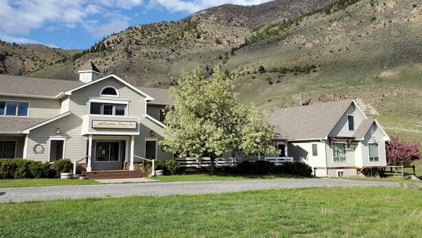 A two-story building with a front porch, a sign indicating it is a guest house, and a view of a mountainous landscape. - Our Cottage Unit-Private end unit of Yellowstone Basin Inn (Gardiner)