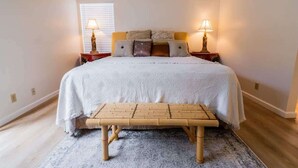 Ein Schlafzimmer mit Bett, Nachttischlampen, einer Bank und einem gemusterten Teppich.