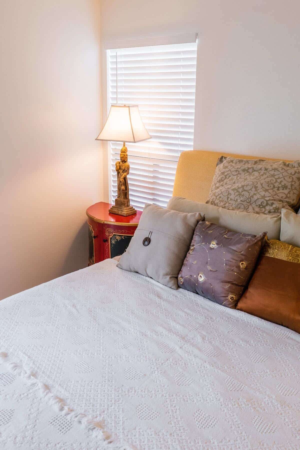 A bedroom with a bed, a nightstand with a lamp, and a window with blinds.