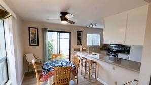 Ein Essbereich mit Tisch und Stühlen, einem Deckenventilator und einer Küchenzeile mit Schränken und Geräten.