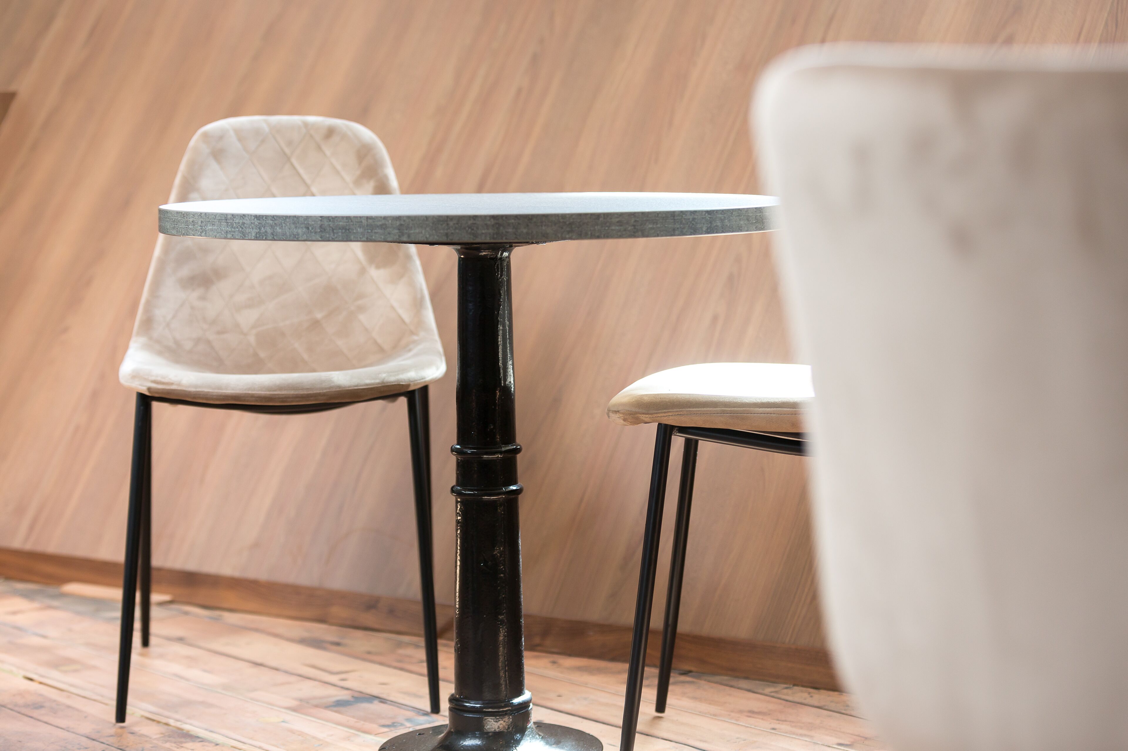 A round table with a black metal base and a beige cushioned chair with a quilted backrest.