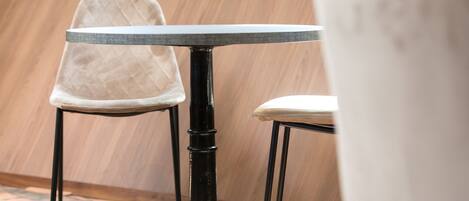 A round table with a black metal base and a beige cushioned chair with a quilted backrest.