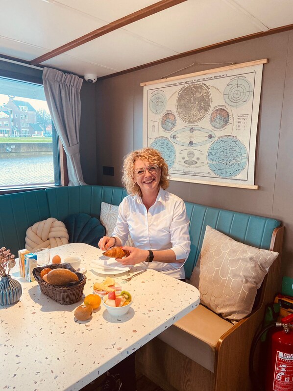 En person sidder ved et bord med et måltid, et kort på væggen og et vindue med udsigt til bygninger.