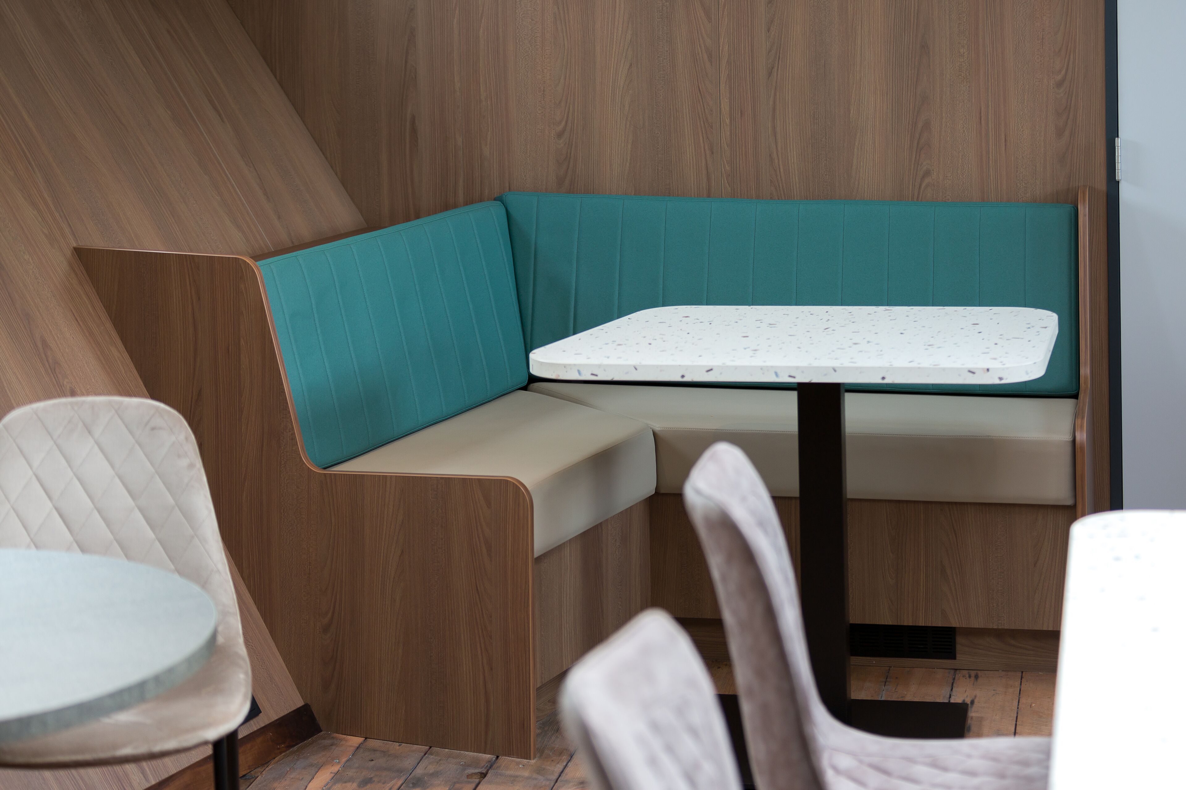 Un intérieur moderne avec un banc recouvert d’un tissu turquoise, une table ronde et un lambris en bois.