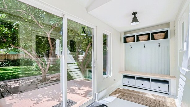 A bright, sunlit room with a sliding glass door leading to a backyard, a bench with storage drawers, and a ceiling light fixture. - Exquisitely Restored Boulder County Victorian Cottage, c1906 🏡 (Longmont)