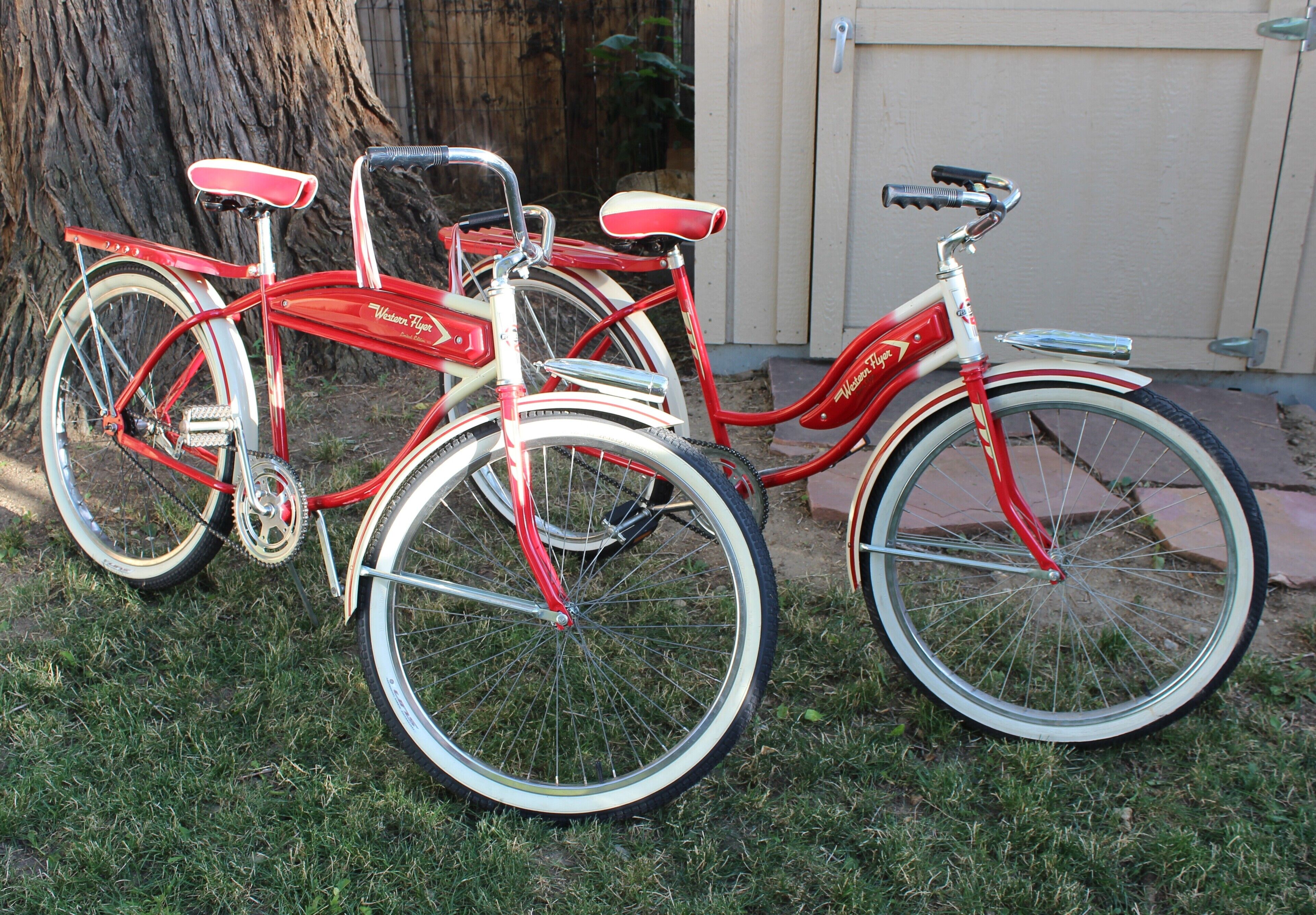 Three vintage bicycles parked on grass next to a wooden tree and a building.