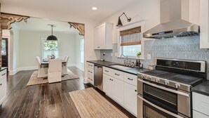 A modern kitchen with white cabinets, a stainless steel range, and a large window with blinds. - Exquisitely Restored Boulder County Victorian Cottage, c1906 🏡 (Longmont)