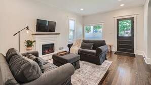 A modern living room with a fireplace, a sofa set, a television, and a large window. - Exquisitely Restored Boulder County Victorian Cottage, c1906 🏡 (Longmont)