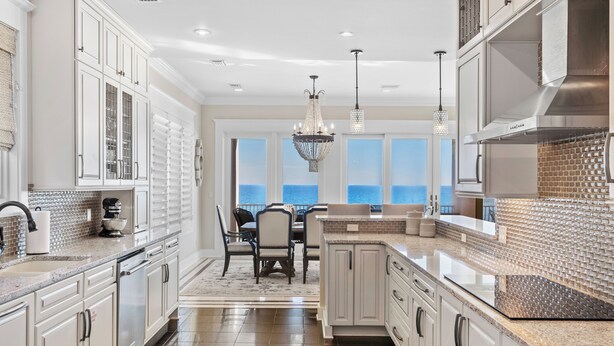 Una cocina moderna con armarios blancos, una isla grande y vista al océano.