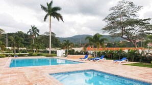 Ein Pool mit zwei Bereichen, umgeben von Palmen und Liegestühlen.