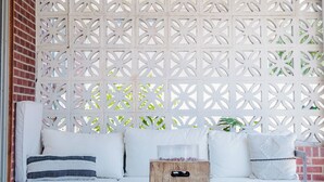 Un espacio de estar al aire libre cubierto con una celosía blanca, un ventilador de techo y una mesa de centro de madera.