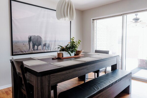 Un comedor moderno con una mesa de madera oscura, un banco y un cuadro grande con elefantes.