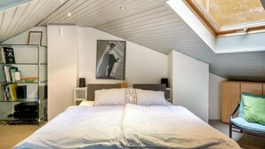 Un dormitorio con una cama grande, tragaluz, una estantería y un cuadro en la pared.
