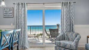 Una habitación con vistas a la playa, un área de comedor con sillas azules y un sillón estampado.
