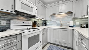 Una cocina moderna con armarios blancos, microondas integrado, extractor de acero inoxidable y salpicadero decorativo.