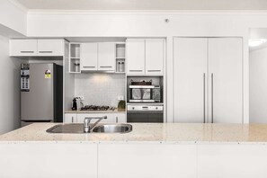 A modern kitchen with white cabinetry, a stainless steel refrigerator, a microwave, and a gas stove.