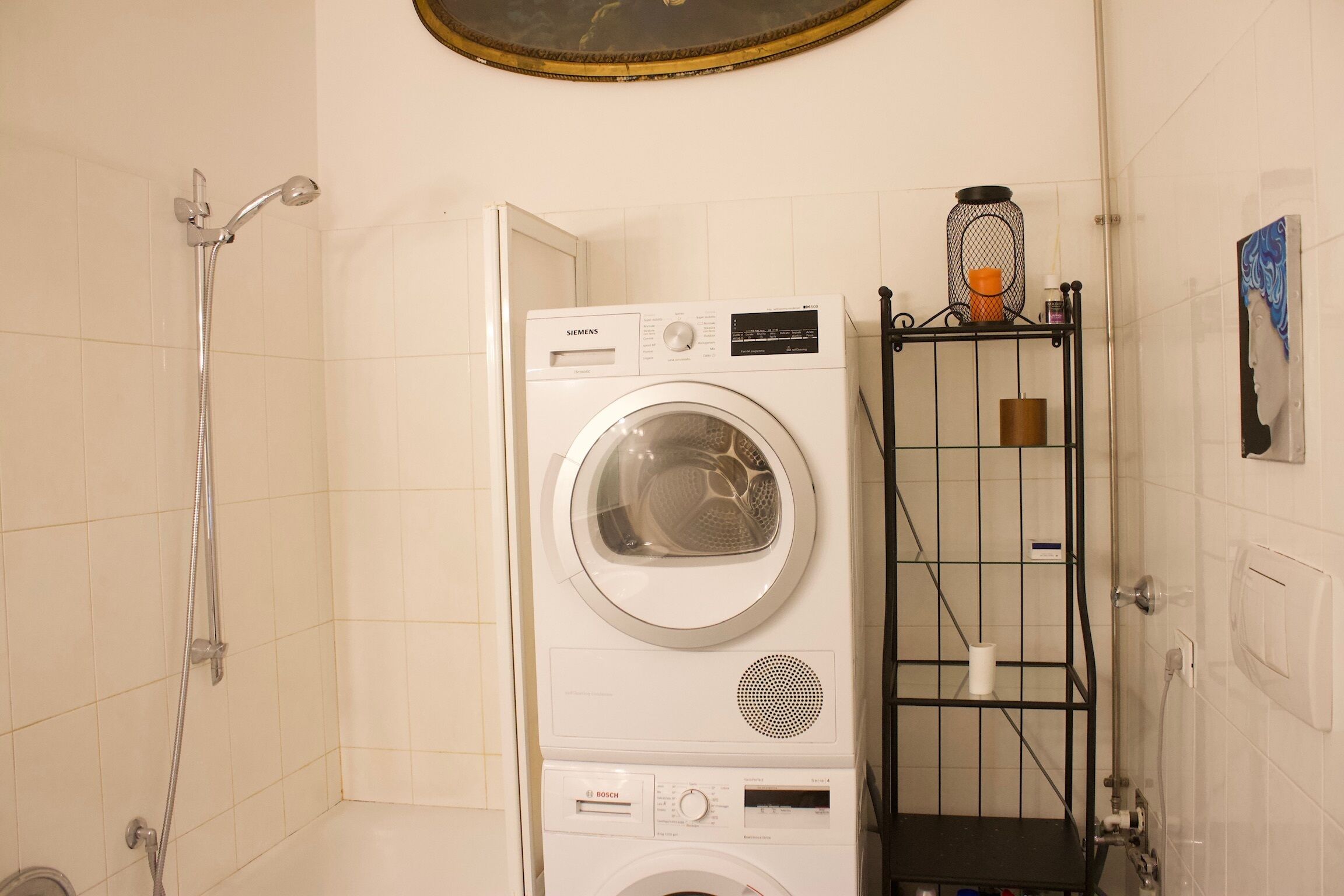 A laundry room with a Siemens and a Bosch washing machine, a shower, and a metal shelf with toiletries.