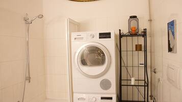 A laundry room with a Siemens and a Bosch washing machine, a shower, and a metal shelf with toiletries.