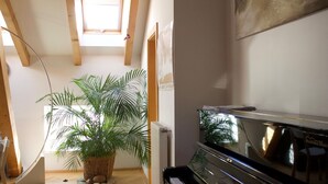 Ein Zimmer mit Klavier, einer großen Kübelpflanze und einer Heizung.