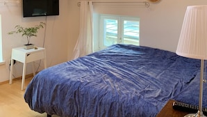 Ein Schlafzimmer mit einem großen Bett, Holzbalken, einem Fernseher, einer Uhr, einem Fenster und einem kleinen Tisch mit einer Pflanze.