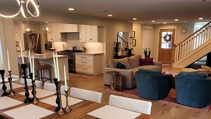 A spacious living room with a wooden dining table, blue ottomans, and a staircase leading to another level. - Corporate rental, great for families in Energy Corridor. (Houston)