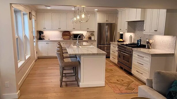 A modern kitchen with white cabinets, a central island, stainless steel appliances, and a dining area with a sofa and coffee table. - Corporate rental, great for families in Energy Corridor. (Houston)