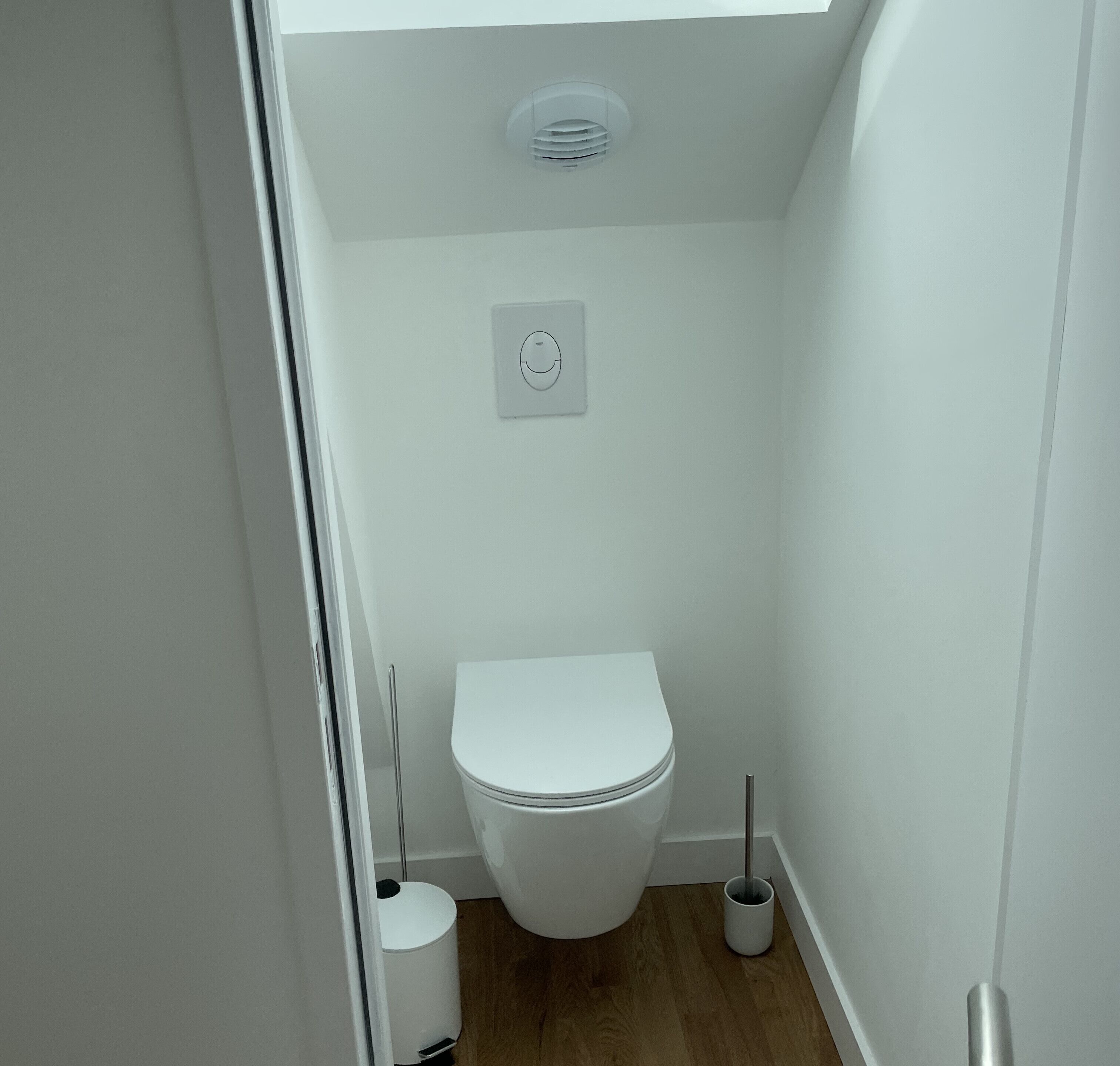Um banheiro pequeno e branco com vaso sanitário, acionador fixado na parede e bidê no chão.