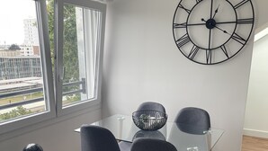 A modern dining area with a glass table, four grey chairs, and a large wall clock. - Poulorio 13 proche gare ★ T2 ★ Dernier Etage * By Locly * (Lorient)