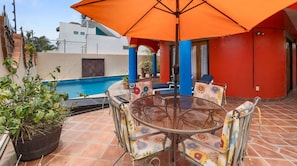 Une terrasse avec une table ronde et des chaises, un pot de fleurs et un parasol orange.