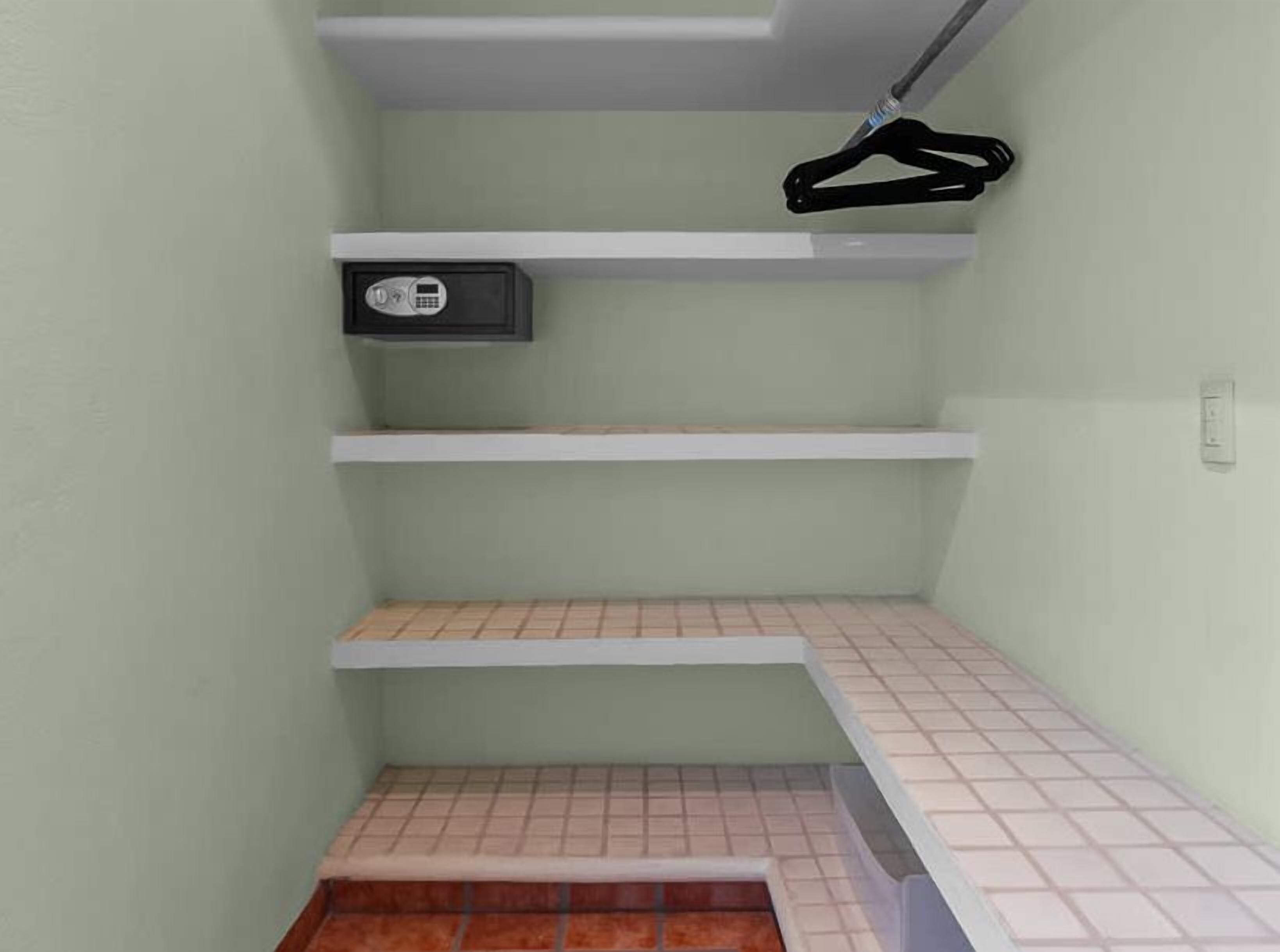 A corner room with a tiled floor, a white shelf, and a black hanger.