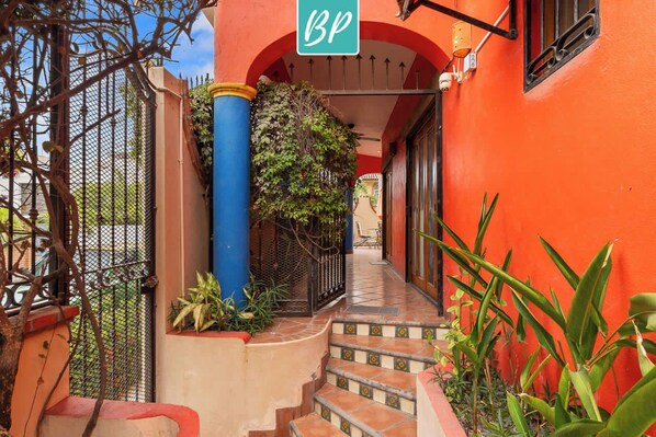 A narrow, tiled corridor with a red wall and a blue pillar, leading to a door with a 'BP' sign.