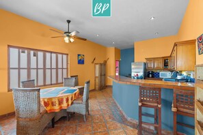 Une cuisine avec un coin bar, une table à manger avec des chaises et un ventilateur de plafond.
