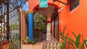 A narrow, tiled corridor with a red wall and a blue pillar, leading to a door with a 'BP' sign. - Golden Zone 2/2 w Pool & Patio (5 Blocks to Beach) (Bucerías)