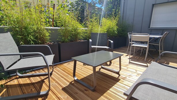 An outdoor patio with metal chairs and a table, surrounded by planters and a wooden deck. - LE POULORIO TERRASSE - T3 RDC - 2 salles de douches  * ByLocly * (Lorient)